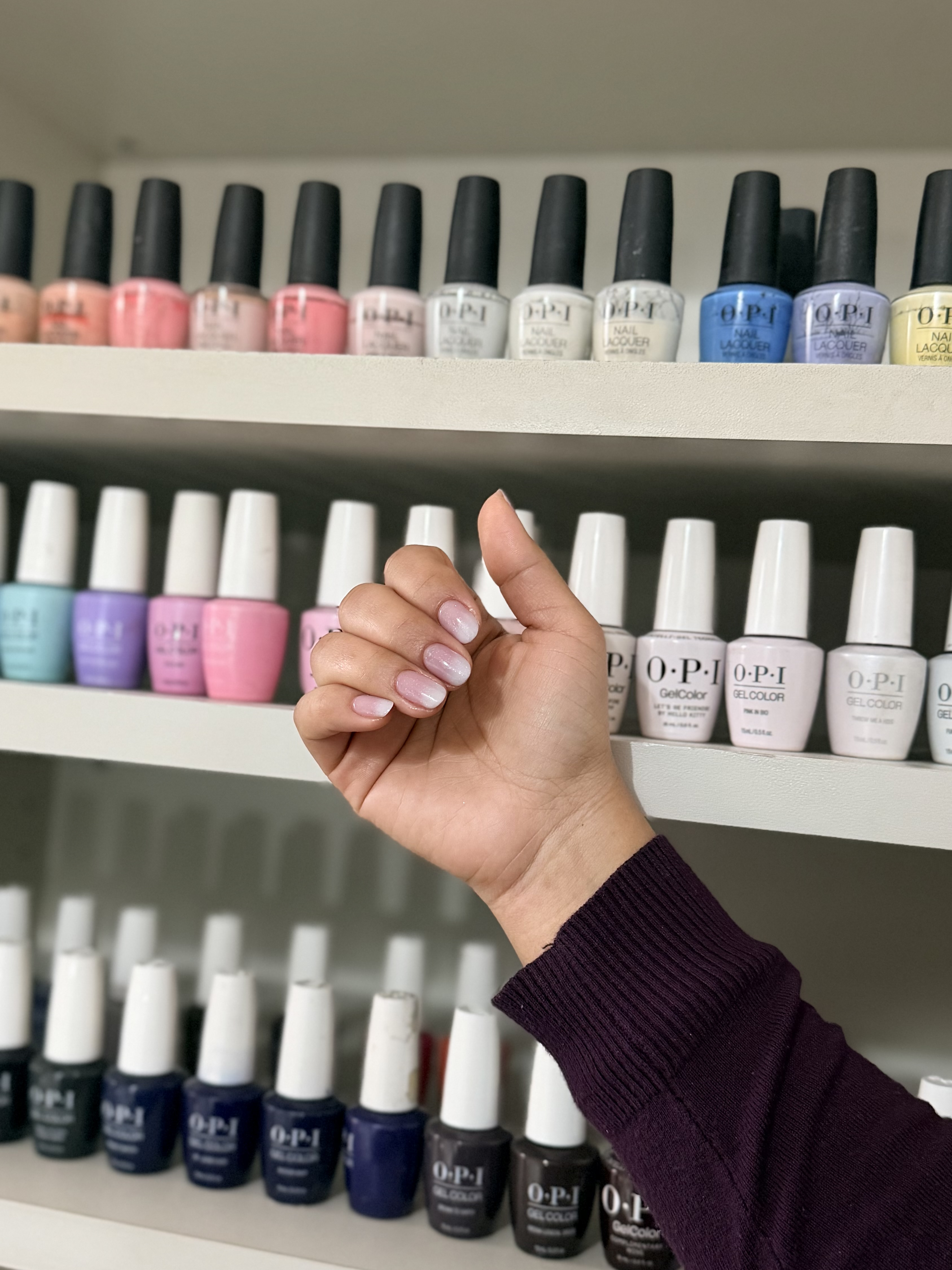 Manicuría en gel rosa nude frente a la pared de esmaltes del salón